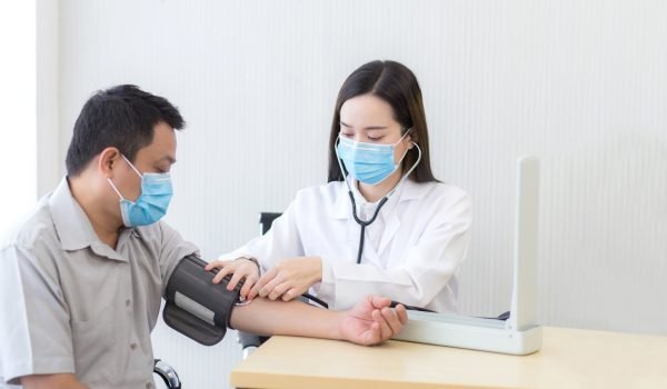Asian female doctor measure blood pressure of a man patient by using a blood pressure meter at hospital while they wear a medical face mask to anti infection of respiratory system.